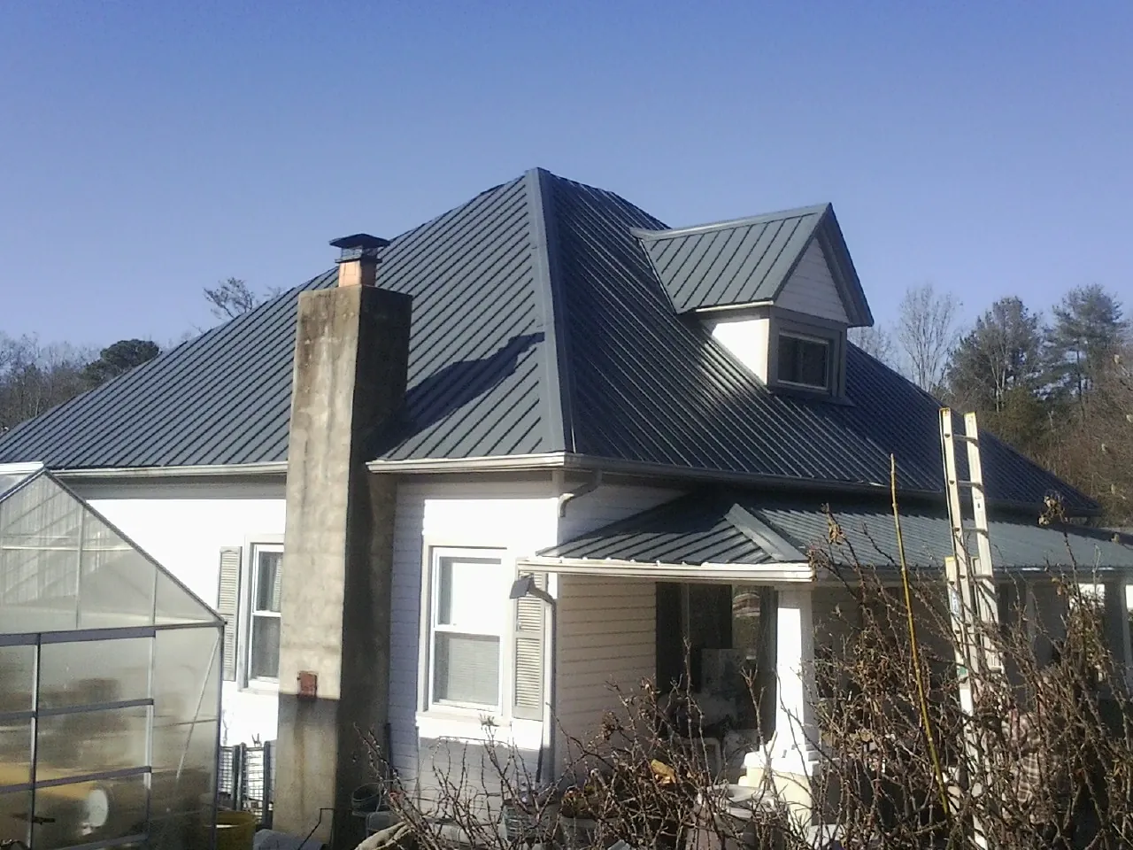 Dark blue standing seam metal roof on a white farmhouse with dormer — Slate & Tile Roof Repair by Roofing Brothers in Bellmore