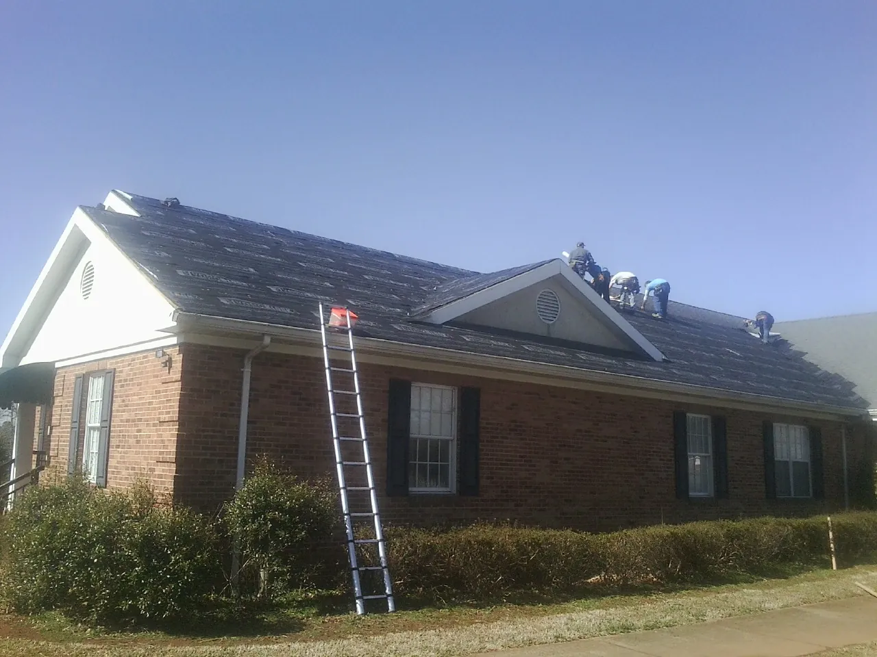 Crew tearing shingles off a brick ranch roof with a ladder set — Metal Roof Repair work by our crew in Bellmore
