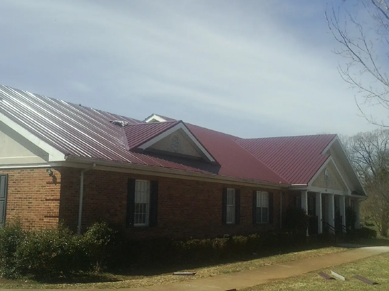 Red metal roof with gabled entries on a long brick building, from a Hail Damage Roof Repair job in Bellmore