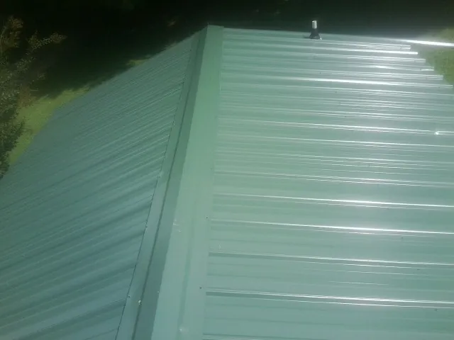 New green metal panels meeting at the ridge of a roof — Flat Roof Repair work by our crew in Bellmore