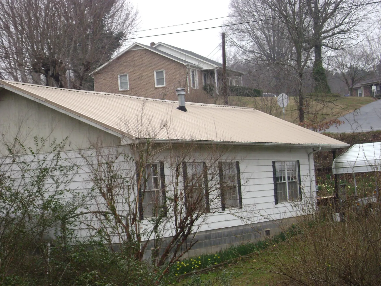 Tan metal roof on a white sided house set into a hillside — Commercial Roofing by Roofing Brothers in Bellmore