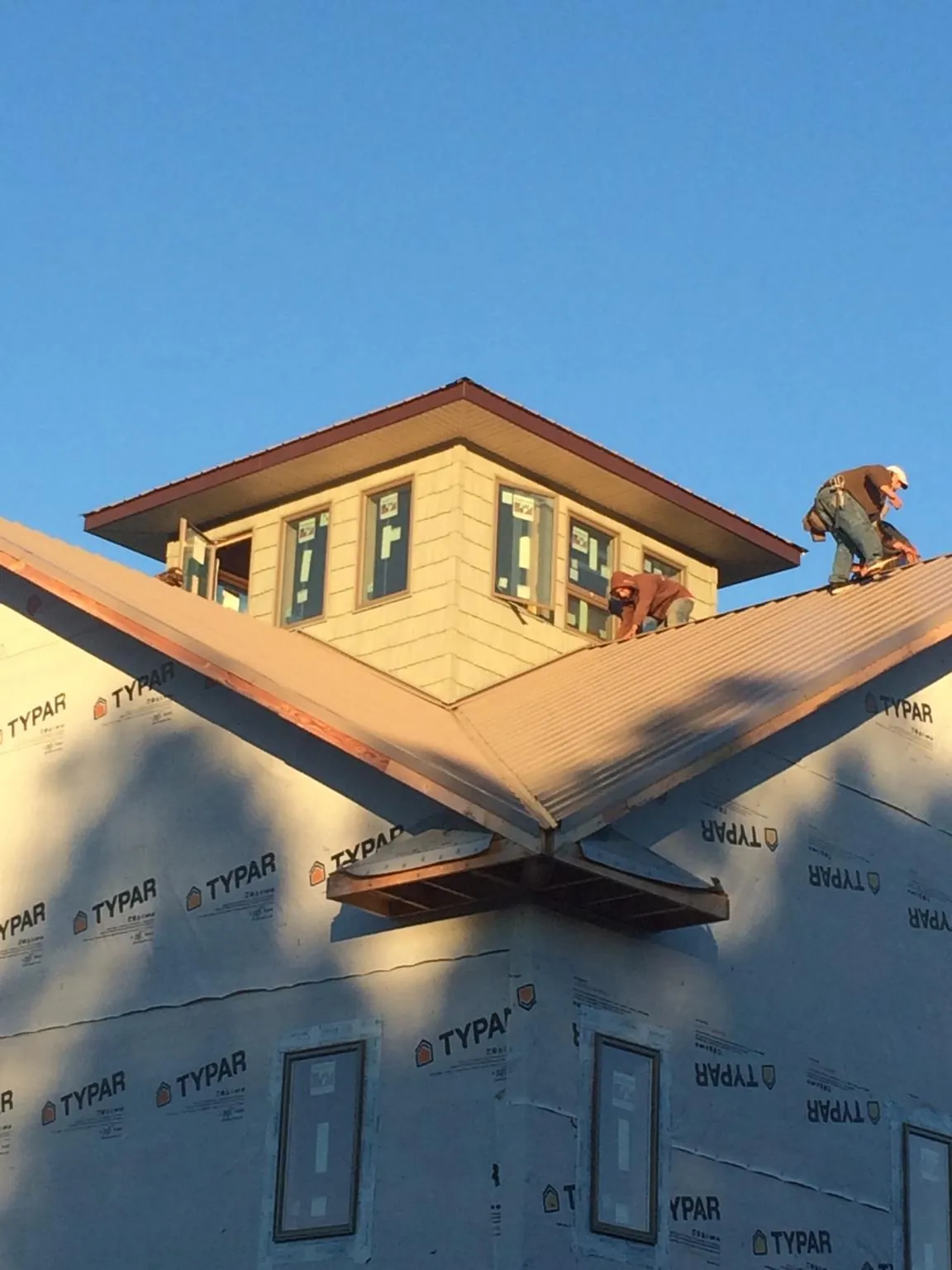 Roofers working around a rooftop cupola on a new metal roof at sunset — Roof Waterproofing in Bellmore by Roofing Brothers